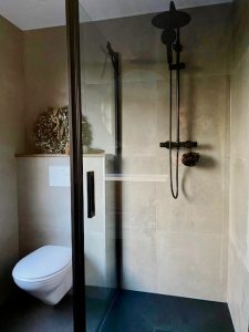 Glazen douchewand landelijke badkamer beige tegels zwarte douchestand krans