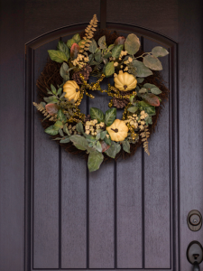 Herfstkrans met kleine pompoenen aan grijze voordeur