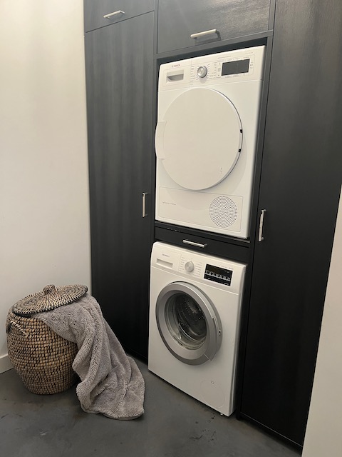 Hotel stijl bijkeuken wasmachine en droger boven elkaar in kastenwand rieten mand met plaid