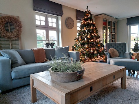 Woonkamer landelijke stijl kerstboom krans aan houten luik olijfbak met windlicht en asparagus
