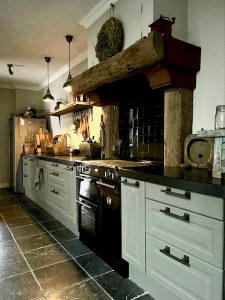 Landelijke keuken met tegelvloer en houten balk boven fornuis gruttersbak hanglampen boven aanrecht