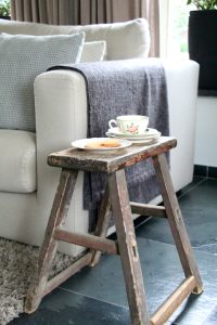 Houten landelijke kruk fauteuil linnen grijze plaid tegel vloer met vloerkleed