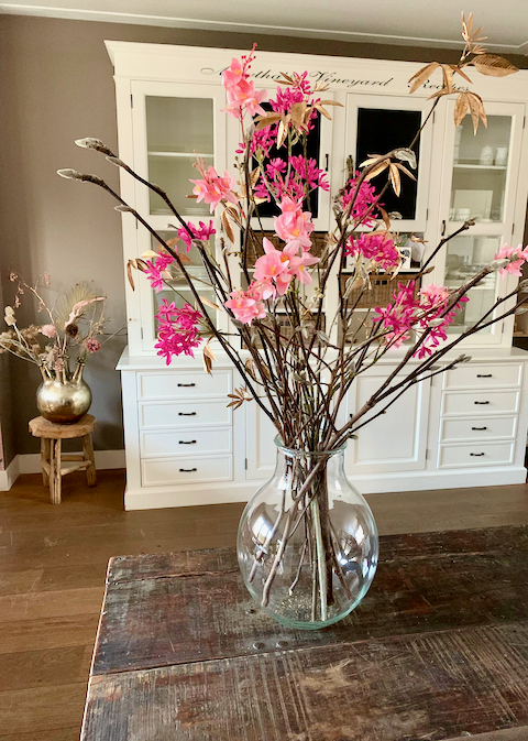 Glazen vaas met roze bloemen toetervaas goud op houten krukje witte buffetkast landelijk