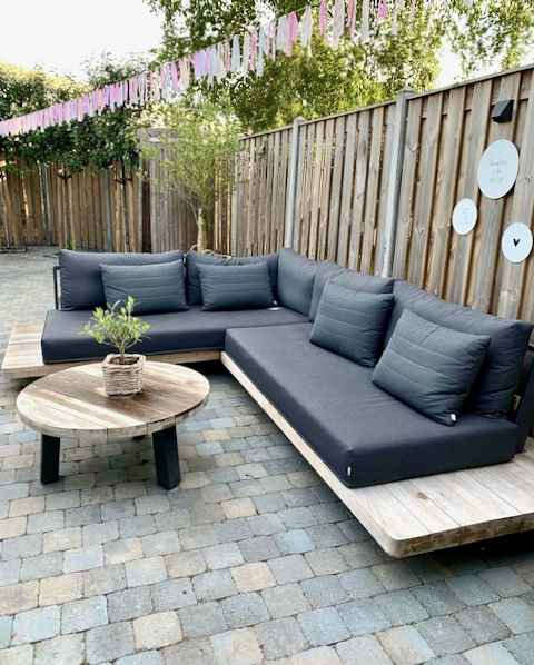 Houten loungeset met grijze tuin kussens ronde salontafel voor buiten roze slinger terras