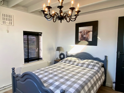 Geblokt dekbedovertrek grijs houten bed antraciet muur decoratie Schotse Hooglander zwarte jaloezieën klein raam slaapkamer