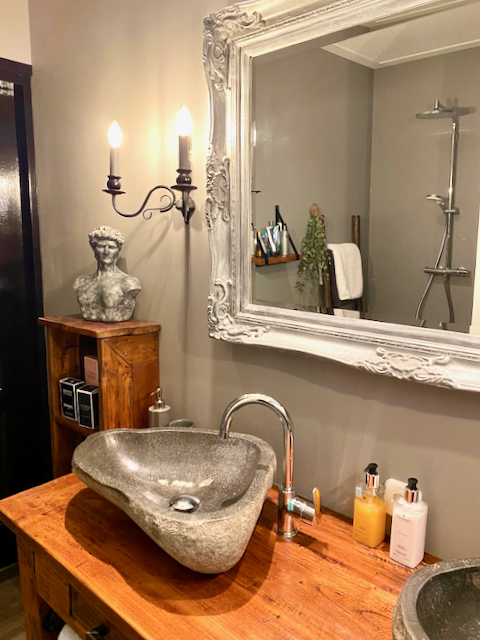 Barok spiegel boven badkamer meubel waskom op houten kastje stenen grijze buste op badkamer kast