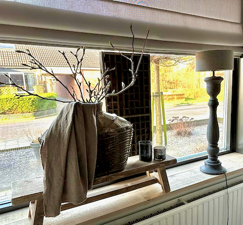 Vensterbank landelijke decoratie houten vensterbank krukje leemkruik met magnolia takken balusterlamp met grijze kap vouwgordijn taupe windlichtje