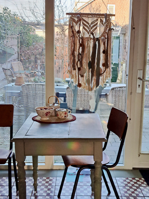 Luxaflex keukenraam houten eettafel voor 2 personen vintage schoolstoelen macramé hanger voor het raam