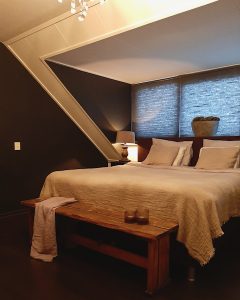 Slaapkamer landelijk ingericht ovale pot met mos houten bankje achter het bed houten balusterlamp op nachtkastje