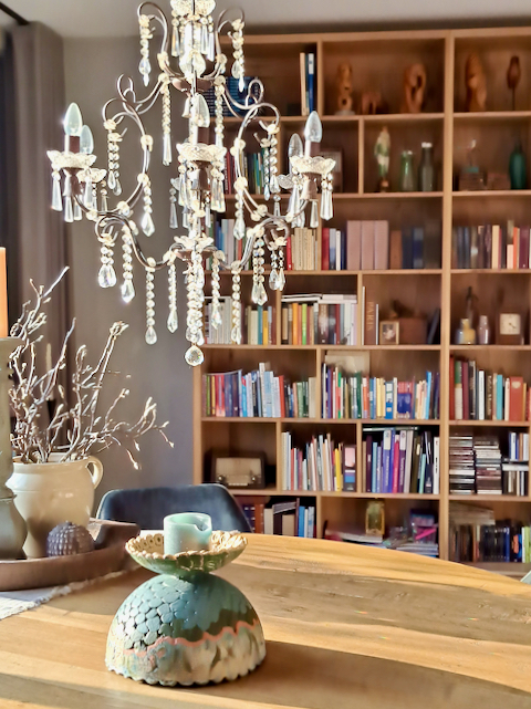 Boekenkast woonkamer kroonluchter met pegels van glas boven eettafel magnoliatakken in kruik op eettafel