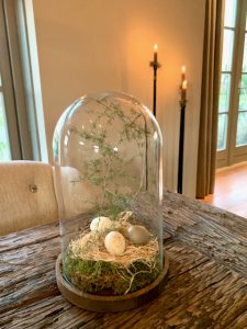 Paas decoratie landelijk glazen stolp met mos en paas eieren en Asparagus takken hoge vloerkandelaars stoere eettafel