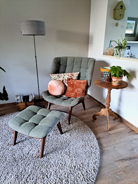 Rond vloerkleed moderne groene fauteuil met hocker grijze vloerlamp wijntafel met bloempot met plant