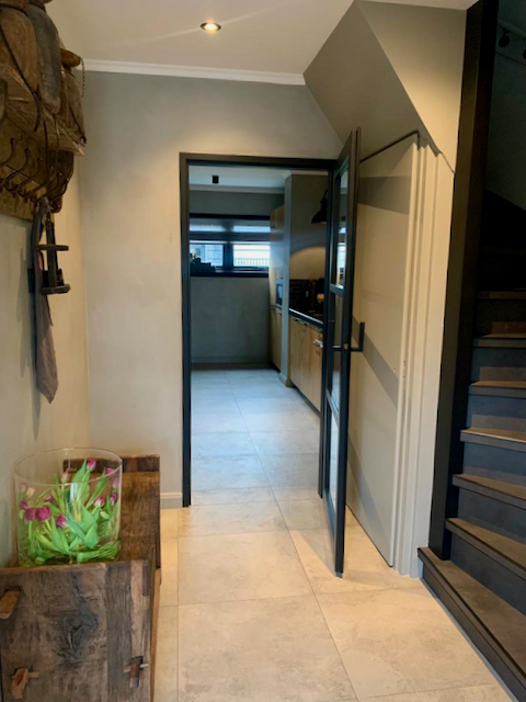 Tussenwoning landelijke hal zwart stalen deur grijze trap houten kapstok met accessoires grote vaas met tulpen
