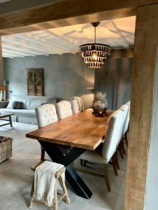 Eetkamer stoelen gecapitonneerd landelijke eethoek schijfjeslamp kalkverf muur houten balk tussen woonkamer en keuken houten kruk met plaid