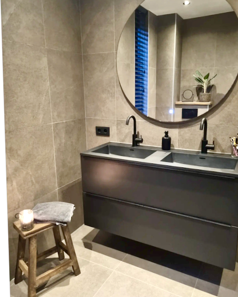 Badkamer meubel bruin grote ronde spiegel houten krukje landelijk zwarte inbouw kranen taupe tegels landelijke badkamer