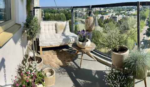 Balkon appartement landelijk ingericht pallet bank potten met balkonplanten rotan windlicht olijfboom op stam jute vloerkleed