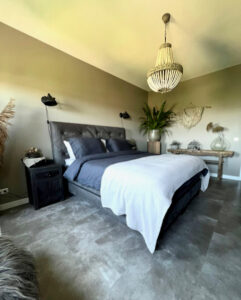 Landelijke slaapkamer in nieuwbouw appartement kroonluchter zuil met plant houten bankje tegen de muur vacht op stok