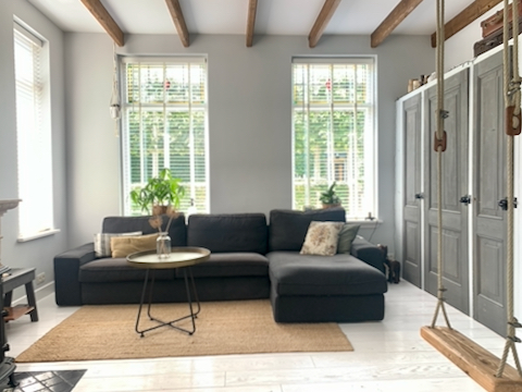 Loungebank sisal vloerkleed inbouwkast woonkamer schommel aan balken plafond witte vloer