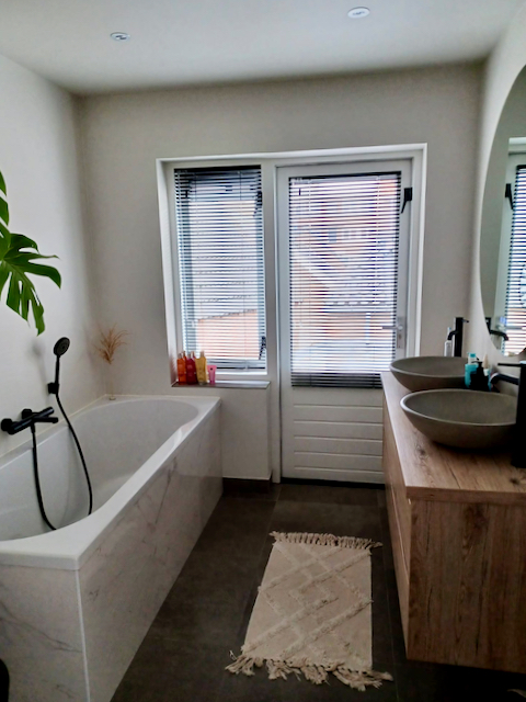 Zwarte jaloezieën badkamer badmeubel hout bad marmer tegels 