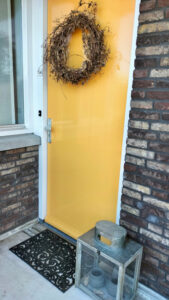 Gele voordeur met landelijke krans windlicht