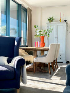 Landelijk met kleur binnenkijken woonkamer appartement lichtblauwe dichte kast oranje vaas klassieke oorfauteuil