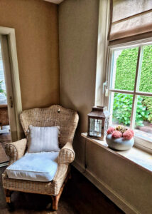 Rotan stoel Riviera Maison vouwgordijn taupe windlicht schaal met gedroogde bloemen op de vensterbank