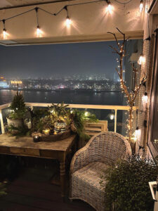 Balkon kerstverlichting rotan tuinstoel houten tafeltje tak met kerst lampjes