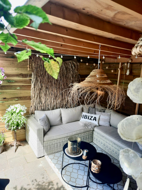 Overkapping Ibiza stijl ingericht raffia lamp ronde salontafels loungebank wanddoek raffia buitenvloerkleed grijs